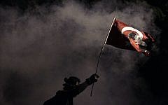 A protester holds a Turkish flag decorated with the image of Turkey's founder Mustafa Kemal Ataturk, during clashes near Taksim Square in Istanbul, late Monday, June 3, 2013 (photo credit: AP/Kostas Tsironis)