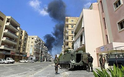 Lebanese army soldiers stand while black smoke rises from a burning house that was attacked during clashes that erupted between followers of a radical Sunni cleric Sheik Ahmad al-Assir and Shiite gunmen in Sidon, Lebanon, Monday, June 24, 2013 (photo credit: AP/Bilal Hussein)
