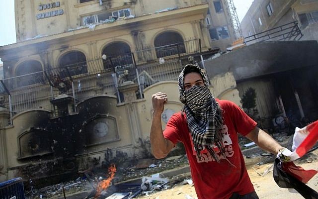 A protester holds an Egyptian flag as he and others attack the headquarters of the Muslim Brotherhood in the Muqattam district of Cairo, Egypt, earlier this month. (photo credit: AP/Khalil Hamra) A protester holds an Egyptian flag as he and others attack the headquarters of the Muslim Brotherhood in the Muqattam district of Cairo, Egypt, earlier this month. (photo credit: AP/Khalil Hamra)