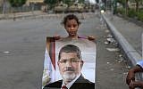 A supporter of ousted Egypt's President Mohammed Morsi poses with his photo as army soldiers guard at the Republican Guard building in Nasr City, in Cairo, Egypt, Wednesday, July 10, 2013 (photo credit: AP/Hassan Ammar)