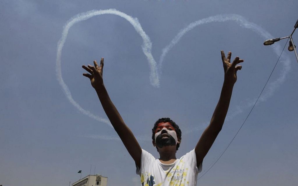 An Egyptian protester flashes V signs for a military aircraft forming a heart-shaped trail in the sky over Tahrir Square in Cairo, Egypt, Friday, July 5. (photo credit: AP/Amr Nabil)