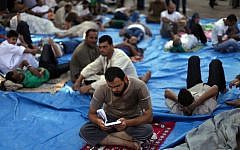 A supporter of ousted president Mohammed Morsi reads the Qur'an, while others rest in the shade during the Ramadan fast as they protest in Nasr City in Cairo, Egypt on Thursday. Pro-Morsi protesters continued their sit-in in front of Rabaah al-Adawiya Mosque in Cairo for the third week, causing residents to complain. (photo credit: AP Photo/Khalil Hamra)