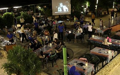 In this picture taken on Wednesday July 24, 2013, Lebanese and Syrian citizens gather at an outdoor coffee shop, as one of the Syrian popular series Al-Wiladah Men Al-Khasira (Birth from the Waist), is broadcast on a giant screen, in Beirut, Lebanon. (photo credit: AP/Hussein Malla)