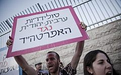An Israeli man holds up a placard that reads, 'Arab-Jewish solidarity against apartheid,' outside a dedication ceremony for the Jewish neighborhood of Maale HaZeitim, inside the Arab-dominated Ras el Amud in East Jerusalem (photo credit: Ruben Salvadori/Flash90)