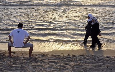 Palestininian women walk by an Israeli man on the beach in Tel Aviv. (photo credit: Serge Attal/Flash90)