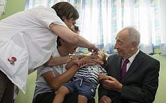 President Shimon Peres (right), watches as a medical worker administers a dose of polio vaccine to a young boy at a clinic in Jerusalem, on Wednesday, August 21, 2013. (photo credit: Flash90)