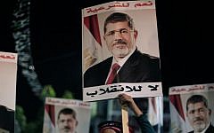 Supporters of Egypt's ousted president Mohammed Morsi hold his posters with Arabic writing which reads 'Yes for legality, No for the coup' during a protest outside Rabaah al-Adawiya mosque on Tuesday. (photo credit: AP/Khalil Hamra)