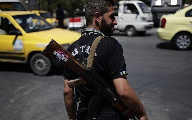 A Syrian soldier holds an AK-47 with a sticker of Syrian President Bashar Assad and Arabic that reads 'Syria is fine,' as he stands guard at a check point on Baghdad street, in Damascus, Wednesday, August 21, 2013. (photo credit: AP/Hassan Ammar) A Syrian soldier holds an AK-47 with a sticker of Syrian President Bashar Assad and Arabic that reads 'Syria is fine,' as he stands guard at a check point on Baghdad street, in Damascus, Wednesday, August 21, 2013. (photo credit: AP/Hassan Ammar)