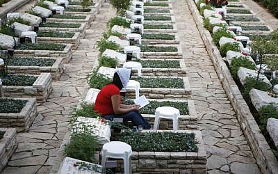 A  woman sits next to the grave of a fallen soldier from the 1973 Yom Kippur War, in the Mount Herzl military cemetery in Jerusalem (Michal Fattal/Flash90)