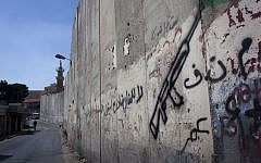 A Palestinian man walks by the barrier separating the West Bank town of Abu Dis from East Jerusalem. The Arabic graffiti, seen on the Abu Dis side, reads, "PLO, no for negotiations." Monday, September 9, 2013. (photo credit: AP/Nasser Nasser)