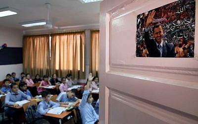 In this Wednesday, Sept. 18, 2013 photo, Syrian pupils attend class at Hassan Shuaib School in Damascus, Syria. A poster on the door depicting President Bashar Assad in Arabic reads,"God is protecting you, Syria." (AP Photo)
