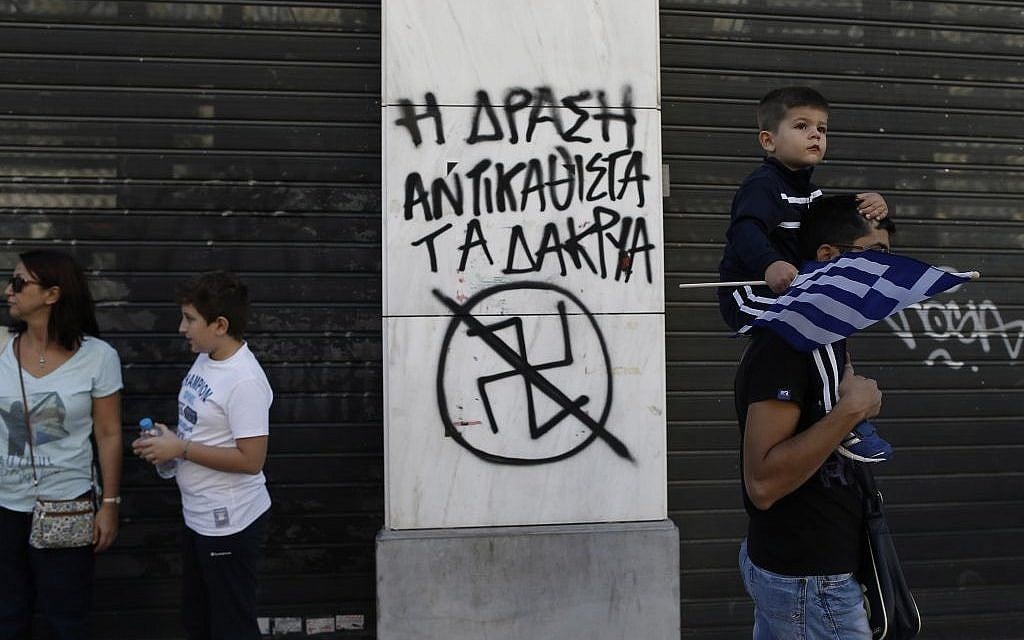 A child holds a Greek flag as he passes with his father next to graffiti depicting an anti Nazi Symbol and reading in Greek 'Action replace tears' during a parade commemorating Greece's entry in World War II in 1940, in central Athens, on Monday, Oct. 28, 2013. (photo credit: AP Photo / Petros Giannakouris) A child holds a Greek flag as he passes with his father next to graffiti depicting an anti Nazi Symbol and reading in Greek 'Action replace tears' during a parade commemorating Greece's entry in World War II in 1940, in central Athens, on Monday, Oct. 28, 2013. (photo credit: AP Photo / Petros Giannakouris)