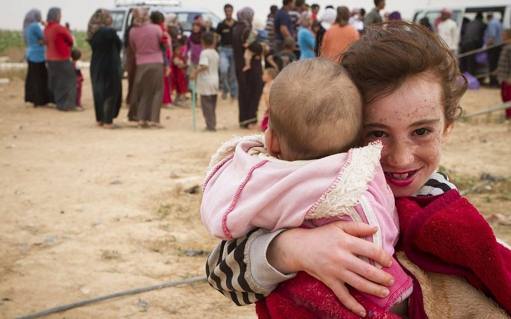 A Syrian refugee child holds her little sister as her family queues for aid behind her. (photo credit: Mickey Alon) A Syrian refugee child holds her little sister as her family queues for aid behind her. (photo credit: Mickey Alon)