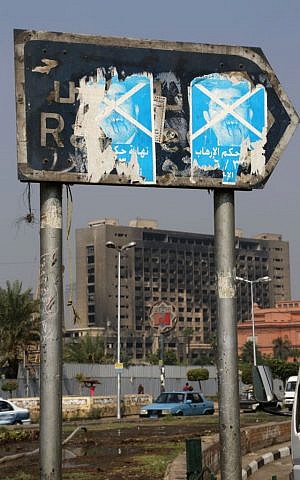 In this Monday, Sept. 30, 2013 photo, torn stickers against Egypt's ousted President Mohammed Morsi cover a street sign in Cairo's Tahrir Square, as the headquarters of the National Democratic Party, which were torched in the 2011 uprising that ousted President Hosni Mubarak loom in the distance. (photo credit: AP/Thomas Hartwell) 