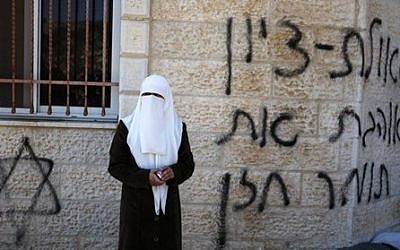 A Palestinian woman stands next to a vandalized mosque in the West Bank village of Burka, near Ramallah, Thursday, Oct. 10, 2013 (photo credit: AP/Majdi Mohammed)