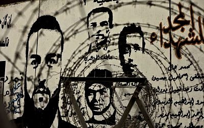 In this file photo taken Sunday, November 17, 2013, murals depicting Egyptian activists who died in anti-government protests look through barbed wire on a wall at Tahrir Square in Cairo, Egypt. Partial translation of the Arabic reads, 'Glory to the martyrs, Abassiya, Tamarod.' (photo credit: AP/Nariman el-Mofty, File)