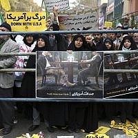 An Iranian woman holds a poster depicting an American diplomat dressed in a jacket and tie, while under the negotiating table he is wearing military pants and pointing a shotgun, as an American flag burns during an annual anti-American demonstration in Tehran, Iran, Monday, Nov. 4, 2013 (photo credit: AP/Ebrahim Noroozi) An Iranian woman holds a poster depicting an American diplomat dressed in a jacket and tie, while under the negotiating table he is wearing military pants and pointing a shotgun, as an American flag burns during an annual anti-American demonstration in Tehran, Iran, Monday, Nov. 4, 2013 (photo credit: AP/Ebrahim Noroozi)