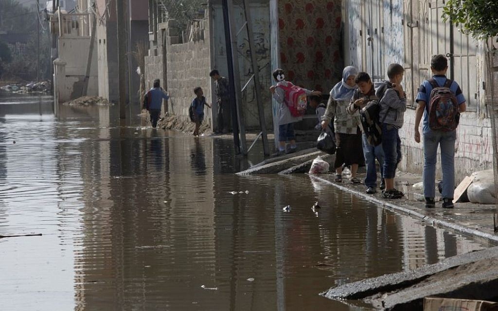 Palestinians walk on the side of a street flooded with waste water in Gaza City, Thursday, Nov. 14, 2013. A Palestinian official said sewage from a treatment plant overflowed onto streets in the Gaza Strip because of a shortage of electricity needed to process the waste. (Photo credit: AP /Adel Hana)