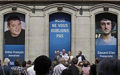 In this file photo taken Tuesday July 9, 2013, Florence Aubenas, holding a microphone at center, a French journalist who was held hostage in Iraq, delivers her speech during a gathering for Europe-1 radio reporter Didier Francois, on the banner at left, and independent photographer Edouard Elias at Europe I radio headquarters in Paris. They have been missing in Syria since the summer. (Photo credit: AP/Remy de la Mauviniere, File)