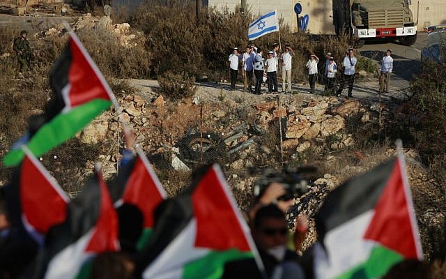Israeli Jewish settlers hold an Israeli flag while Palestinian protesters wave Palestinian flags during a protest against the Prawer Plan, near the Israeli settlement of Beit El on Saturday, November 30, 2013. (photo credit: AP/Majdi Mohammed)