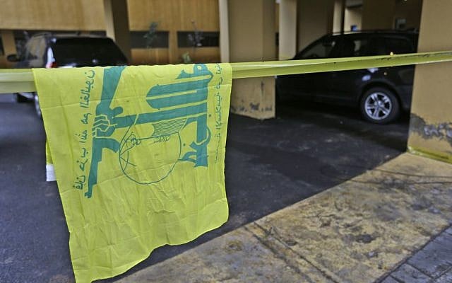 A Hezbollah flag hangs on yellow police tape sealing off the scene where Hassan al-Laqis, a senior commander for the Lebanese militant group Hezbollah, was gunned down outside his home, some two miles (three kilometers) southwest of Beirut, Lebanon on Wednesday, December 4, 2013.  (photo credit: AP/Hussein Malla)