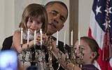 President Barack Obama holds up Kylie Schmitter as she, alongside her sister Lainey Schmitter, lights the menorah during the first of two Hanukkah receptions in the White House, on Thursday, December 5, 2013. (photo credit: AP/Carolyn Kaster)