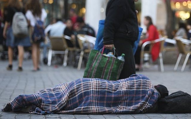 People walk by a homeless man sleeping on the street, in the center of Jerusalem, on November 10, 2013. (photo credit: Nati Shohat/Flash90)
