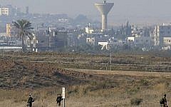 Palestinian demonstrators protest near the Israeli border fence with Gaza (unseen) as Israeli army soldiers patrol on the border, January 3, 2014. A Gaza water tower can be seen in the background. (photo credit: David Buimovitch/Flash90)