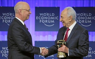 President Shimon Peres and Klaus Schwab the founder and Executive Chairman of the World Economic Forum shake hands as Peres holds an award from the WEF honoring him for his long-standing commitment to its mission, at the annual meeting of the WEF in Davos, January 24, 2014. (Photo credit: World Economic Forum/HANDOUT/Flash90)