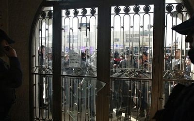 Palestinian protesters look through broken glass doors of a gate at a hotel where a group of Israelis and Palestinians hold a meeting in the West Bank city of Ramallah, Thursday, January 9, 2014. (photo credit: AP Photo/Majdi Mohammed)