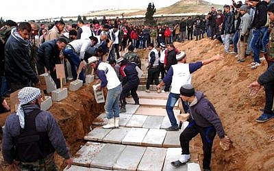Syrian citizens bury in a mass grave the bodies of victims who were killed Thursday by a car bomb in Hama province, Syria, on Friday (photo credit: AP/SANA)
