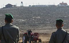 Israeli Border Police officers stand guard as Palestinian farmers use tractors to work the land in the village of Qusra in the West Bank, with the Esh Kodesh outpost in the background, on November 19, 2013. (Nati Shohat/Flash90)