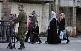 Arab women walk by an Israeli soldier patrolling in the divided West Bank city of Hebron. (photo credit: Miriam Alster/Flash90)