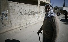 A resident of an East Jerusalem neighborhood walks past graffiti 'Arab labor = assimilation,' Monday, February 10, 2014 (photo credit: Flash90)