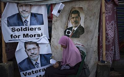 A supporter of Egypt's ousted president Mohammed Morsi reads the Quran as she sits next to a tent with posters of Morsi in Cairo, Egypt, in August.  (photo credit: AP/Khalil Hamra)