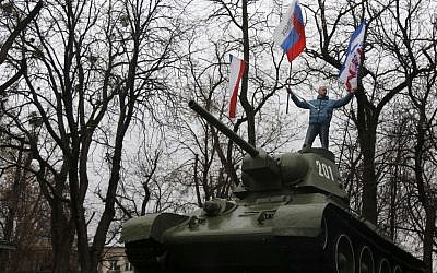 A Pro-Russian demonstrator waves Russian and Crimea flags from an old Soviet Army tank during a protest in front of a local government building in Simferopol, Crimea, Ukraine, on Thursday, February 27, 2014. (photo credit: AP Photo/Darko Vojinovic)