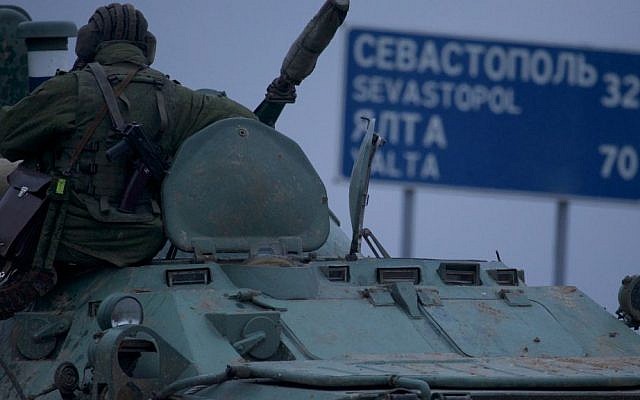 A soldier rests atop a Russian armored personnel carrier with a road sign reading "Sevastopol - 32 kilometers, Yalta - 70 kilometers", near the town of Bakhchisarai, Ukraine, Friday, Feb. 28, 2014. (photo credit: AP/Ivan Sekretarev)