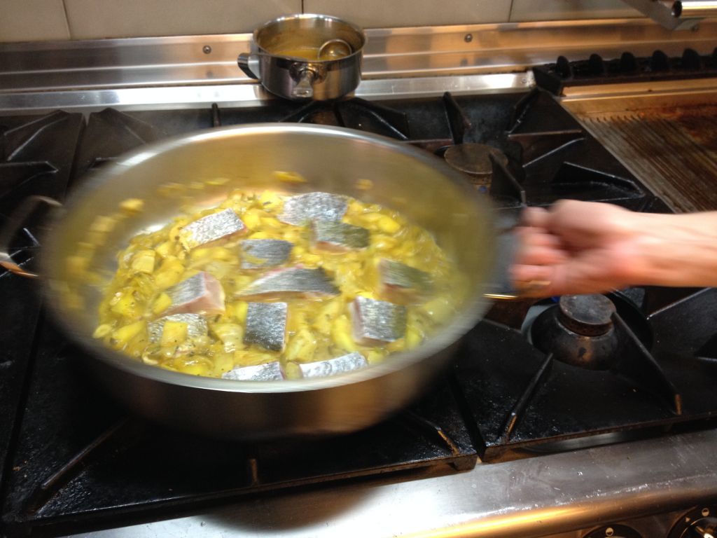 Shaking a pan of artichokes, fennel and fish poaching on the flame (photo credit: Jessica Steinberg/Times of Israel)