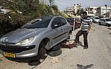 Illustrative: A Palestinian man changes the tires of his car after a 'price tag' attack in March 2014 (photo credit: AFP/Ahmad Gharabli)