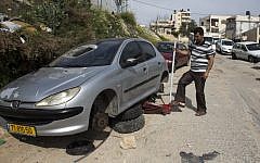 Illustrative: A Palestinian man changes the tires of his car after a 'price tag' attack in March 2014 (photo credit: AFP/Ahmad Gharabli)