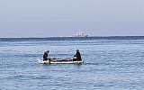 Palestinian fishermen sit in their boat off the shores of the southern Gaza Strip town of Rafah, as an Israeli patrol is seen in the distance, March 26, 2014. (AFP/Said Khatib)