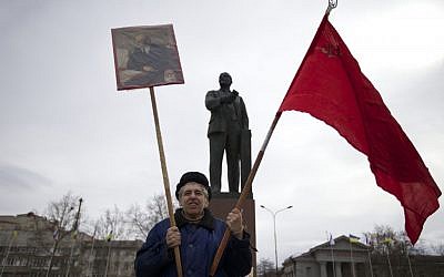 A local Communist party supporter holds Soviet flag and portrait of Soviet founder Vladimir Lenin as he stands next to Lenin's statue at a square in downtown Simferopol, Ukraine. (photo credit: AP Photo/Ivan Sekretarev)