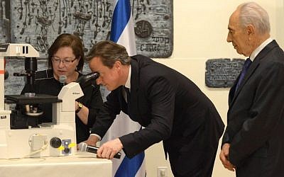 British Prime Minister David Cameron looks through a microscope at half-developed embryonic stem cells as Dr. Sharona Even-Ram of the Hadassah Medical Center tells him and President Shimon Peres about how the cells can be used to treat Parkinson's disease during a research exhibition at Beit HaNassi Wednesday evening. (Photo credit: Mark Neiman/GPO)