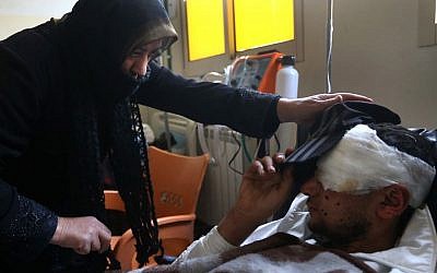 Ibrahim, 18, a Syrian rebel who lost one of his eyes during a battle against government forces and Hezbollah fighters in Rima village near Yabroud, lies on his bed as his aunt helps him to put hat on his head, at a makeshift hospital in the Lebanese-Syrian border town of Arsal, eastern Lebanon on Wdnesday, March 5, 2014.  (photo credit: AP/Hussein Malla)