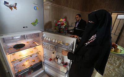 Ahmed Zeitouniya, 32, an employee of the Culture Ministry, helps his wife Minatullah, 29, prepare food in the kitchen of their house in Gaza City in the northern Gaza Strip. Their fridge has been rather empty since Ahmed has not received his salary for the month.(photo credit: AP Photo/Hatem Moussa)