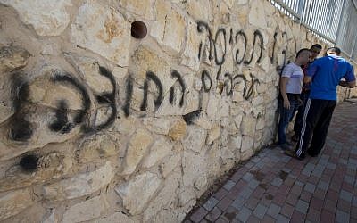 Arab Israeli men stand next to graffiti reading in Hebrew "Arabs Out" on the wall of a mosque in the northern Israeli city of Umm al-Faham on April 18, 2014. (photo credit: AFP/ JACK GUEZ)