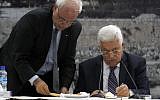 Palestinian Authority President Mahmoud Abbas, right, signs a request to join 15 United Nations-linked and other international treaties at his headquarters in the West Bank city of Ramallah on Tuesday, April 1, 2014. Standing next to him is Saeb Erekat. (Issam Rimawi/Flash90)