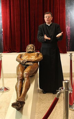 Father Eamon Kelly describes a sculpture depicting the man of the Shroud of Turin (photo credit: Rebecca McKinsey/The Times of Israel)