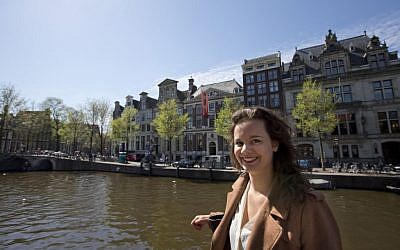 In this Wednesday April 16, 2014 photo, Charlotte van den Berg poses for a portrait outside the NIOD Institute for War, Holocaust and Genocide Studies, rear, in Amsterdam, Netherlands. Charlotte van den Berg was a 20-year-old college student working part-time in Amsterdam’s city archives when she and other interns came across a shocking find: letters from Jewish Holocaust survivors complaining that the city was forcing them to pay back taxes and late payment fines on property seized after they were deported to Nazi death camps. Van den Berg waged a lonely fight against Amsterdam’s modern bureaucracy to have the travesty publicly recognized. Now, largely due to her efforts, Amsterdam officials are considering compensating Holocaust survivors for the taxes and possibly other obligations, including gas bills, they were forced to pay for homes that were occupied by Nazis or collaborators while the rightful owners were in hiding or awaiting death in the camps. (photo credit: AP/Peter Dejong)