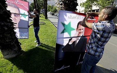 Syrian men hang election campaign billboards bearing portraits of President Bashar al-Assad in a street of the capital Damascus, May 11, 2014. (photo credit: AFP/JOSEPH EID)